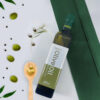 A bottle of Zuriyat extra virgin olive oil with green olives and a wooden spoon