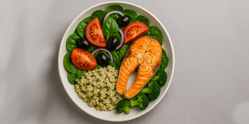 A plate of salmon, quinoa, spinach, tomatoes, black olives and broccoli