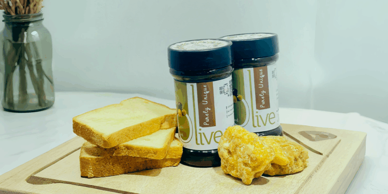 Two jars of Zuriyat olive jam on a wooden board with slices of bread and gur