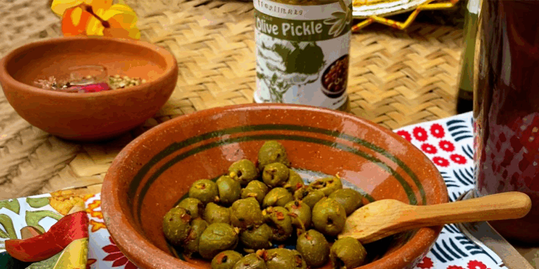 Pickled olives in a clay bowl with a wooden spoon, a jar of olive pickle behind